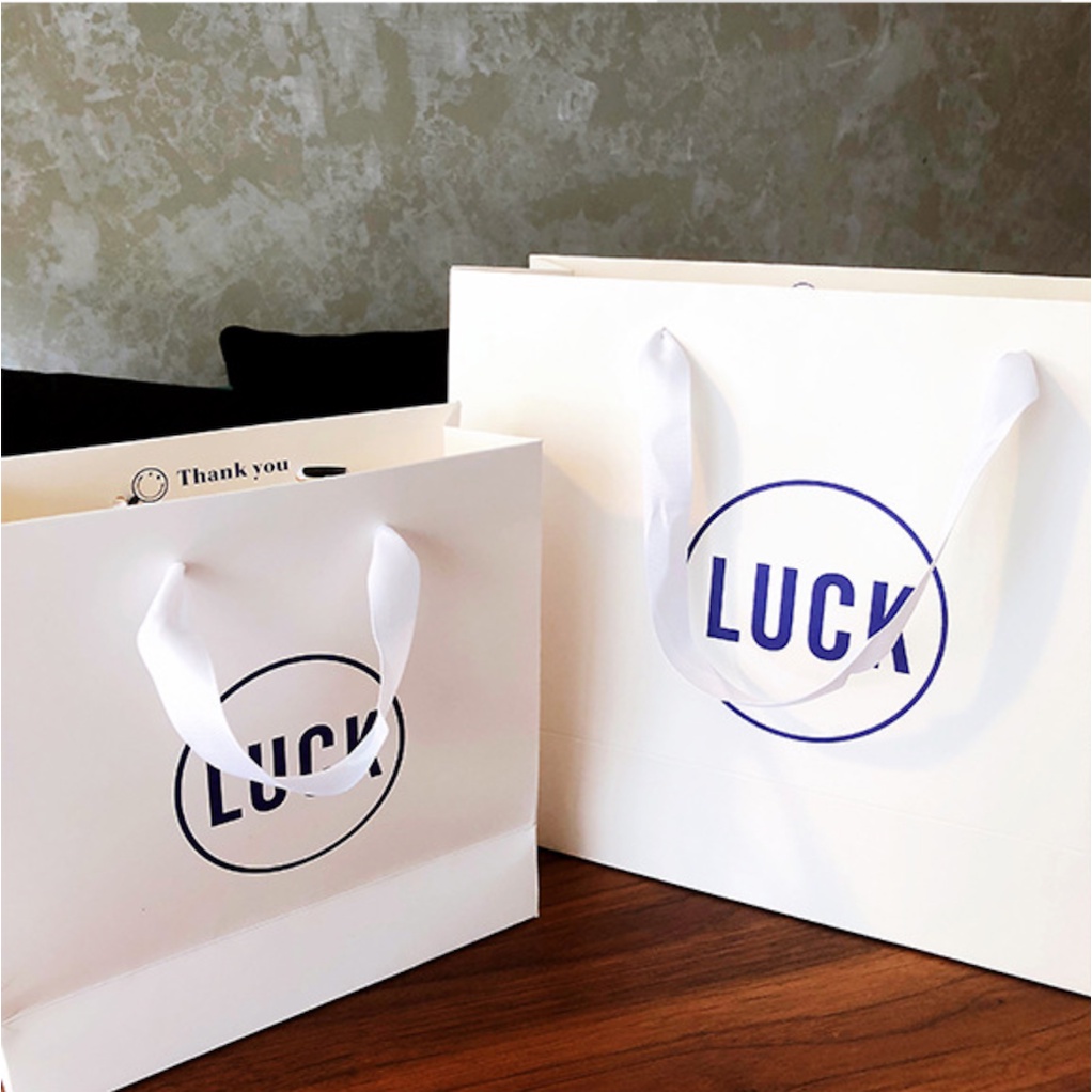 Túi giấy bìa cứng trắng logo "I DO" và "LUCK" màu xanh, quai vải mềm