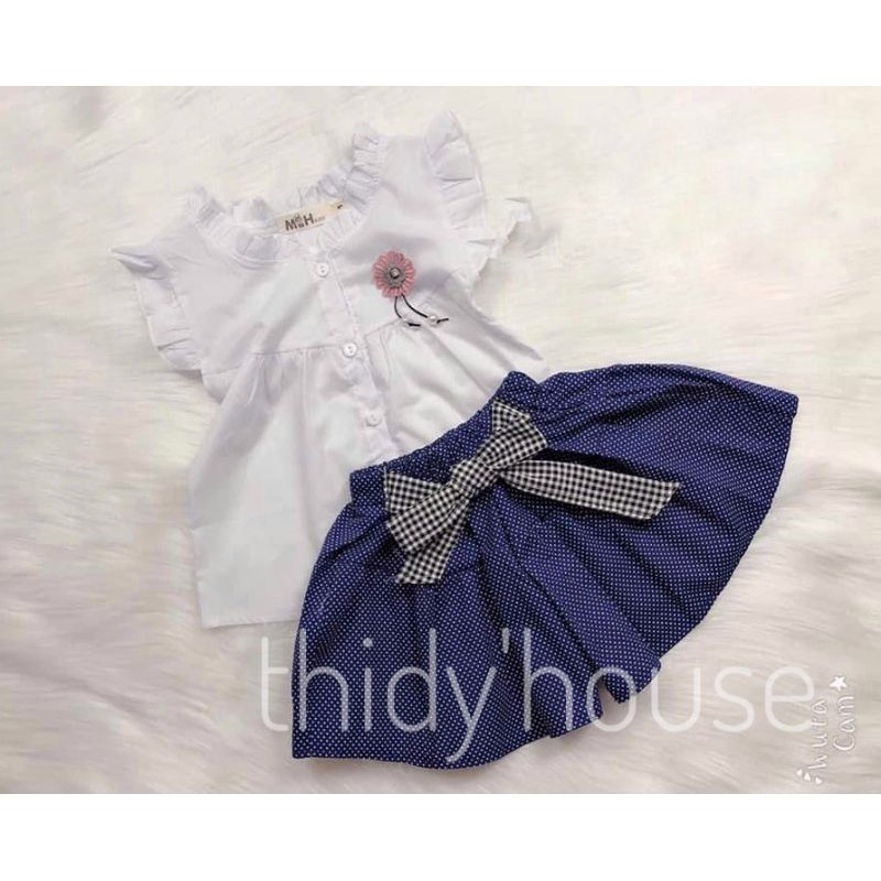 Set áo sơmi trắng có tag hoa đính ngực kết hợp cùng quần xanh chấm bi giả váy phối nơ, size cho bé gái từ 12 - 25kg