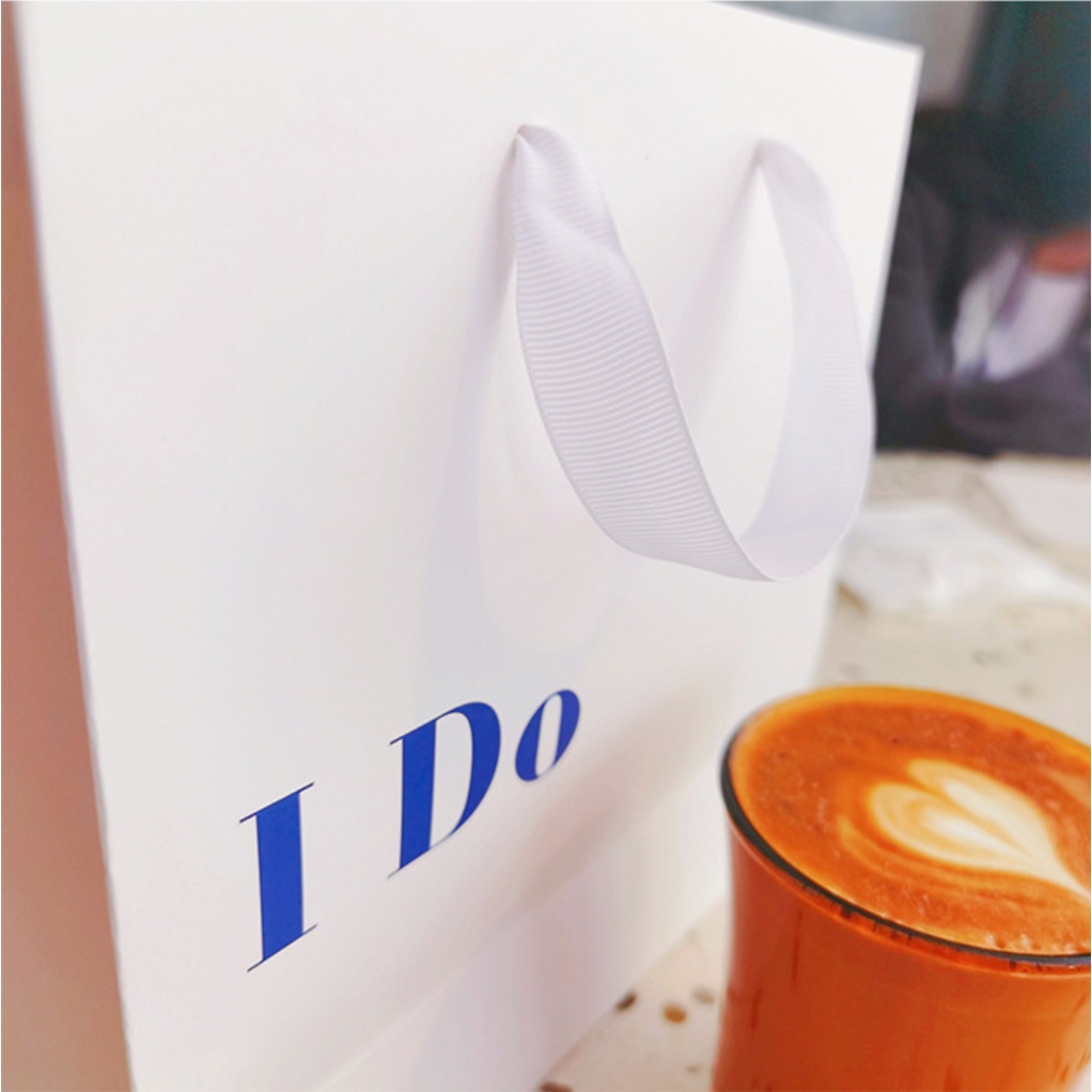 Túi giấy bìa cứng trắng logo "I DO" và "LUCK" màu xanh, quai vải mềm