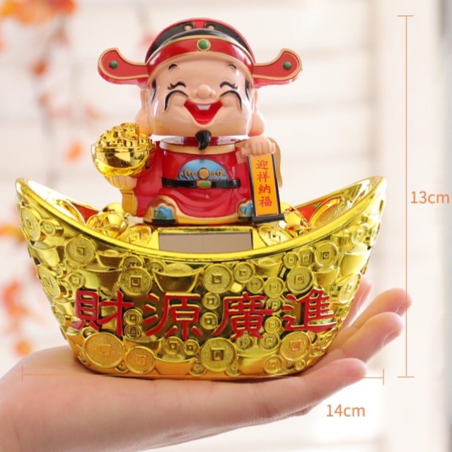 Tượng thần tài áo đỏ đứng trên ngân lượng phong thủy, gật đầu bằng năng lượng mặt trời