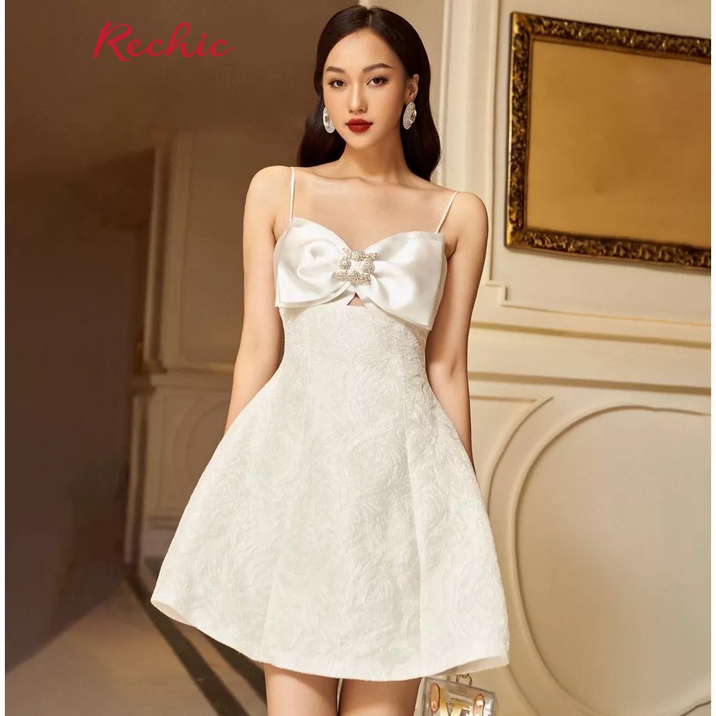 RECHIC Đầm Evita Màu Trắng hai dây đính nơ đá nơ ngực dáng ngắn chất liệu Gấm sang trọng