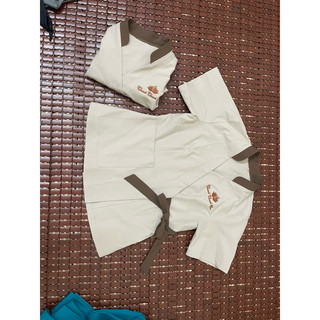 Bộ đồng phục spa, nền màu da, né cổ và nơ màu nâu, quần dài.